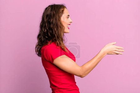 Photo for Young pretty woman smiling, greeting you and offering a hand shake to close a successful deal, cooperation concept - Royalty Free Image