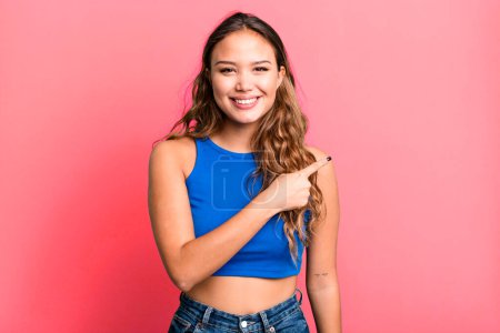 Photo for Young pretty woman smiling cheerfully, feeling happy and pointing to the side and upwards, showing object in copy space - Royalty Free Image