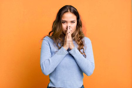 Foto de Joven bonita mujer sintiéndose preocupada, esperanzada y religiosa, orando fielmente con las palmas presionadas, rogando perdón - Imagen libre de derechos