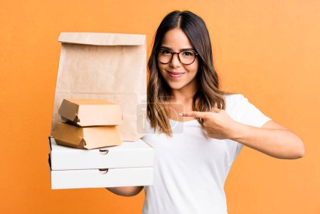 Foto de Hispanic pretty woman smiling cheerfully, feeling happy and pointing to the side. delivery and take away fast food concept - Imagen libre de derechos
