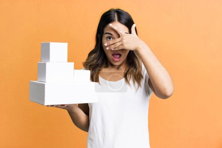 Photo for Hispanic pretty woman looking shocked, scared or terrified, covering face with hand with blank packages boxes - Royalty Free Image