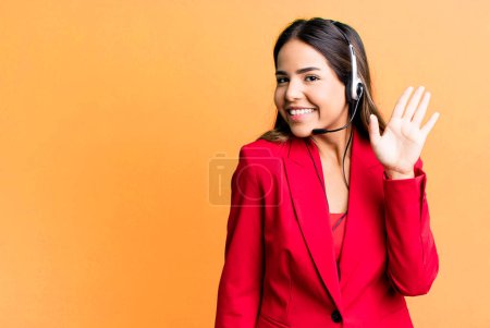 Foto de Hispanic pretty woman smiling happily, waving hand, welcoming and greeting you. telemarketing concept - Imagen libre de derechos