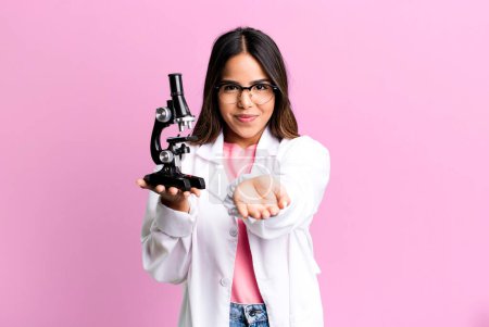 Photo for Hispanic pretty woman smiling happily with friendly and  offering and showing a concept. scients student with a microscope - Royalty Free Image