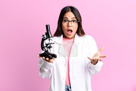 Foto de Hispanic pretty woman feeling extremely shocked and surprised. scients student with a microscope - Imagen libre de derechos