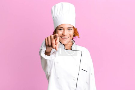 Téléchargez les photos : Red hair pretty woman pointing at camera choosing you. chef concept - en image libre de droit