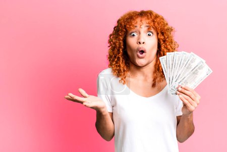 Photo for Red hair pretty woman feeling extremely shocked and surprised. dollar banknotes and money concept - Royalty Free Image