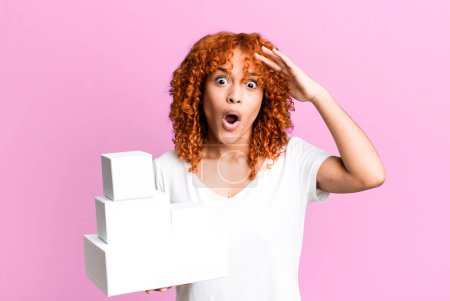 Téléchargez les photos : Cheveux roux jolie femme regardant heureux, étonné et surpris. concept de boîtes de paquets vides - en image libre de droit