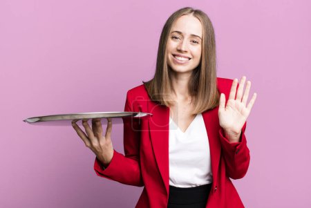 Photo for Smiling happily, waving hand, welcoming and greeting you. businesswoman presenting with a tray - Royalty Free Image