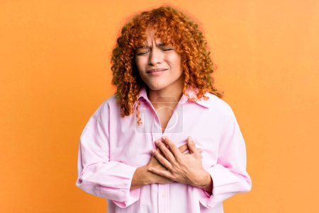 Photo for Redhair pretty woman looking sad, hurt and heartbroken, holding both hands close to heart, crying and feeling depressed - Royalty Free Image
