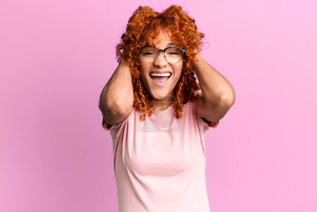 Photo for Redhair pretty woman raising hands to head, open-mouthed, feeling extremely lucky, surprised, excited and happy - Royalty Free Image