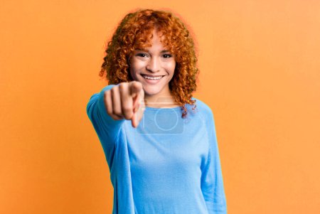 Photo for Redhair pretty woman pointing at camera with a satisfied, confident, friendly smile, choosing you - Royalty Free Image