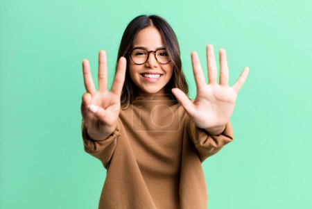Photo for Hispanic pretty woman smiling and looking friendly, showing number eight or eighth with hand forward, counting down - Royalty Free Image