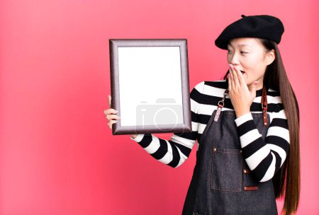 Foto de Young adult pretty asian woman with a beret and an empty picture frame - Imagen libre de derechos