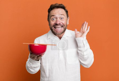 Photo for Middle age man feeling happy and astonished at something unbelievable. breakfast bowl - Royalty Free Image