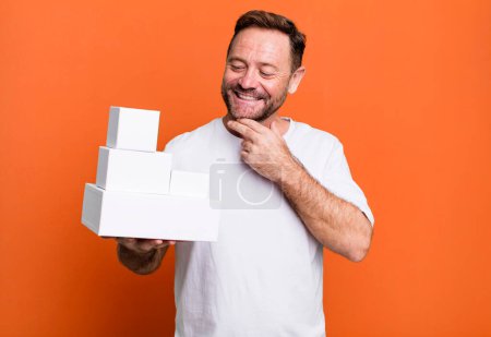 Photo for Middle age man smiling with a happy, confident expression with hand on chin. blank packages concept - Royalty Free Image