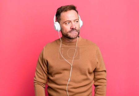 Foto de Middle age man feeling sad, upset or angry and looking to the side. listening music with a headphones - Imagen libre de derechos