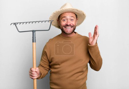 Photo for Middle age man feeling happy, surprised realizing a solution or idea. farmer with a rake - Royalty Free Image