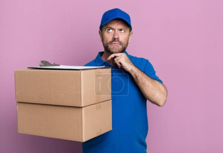 Foto de Middle age man thinking, feeling doubtful and confused. paker delivery man. packer delivery man - Imagen libre de derechos