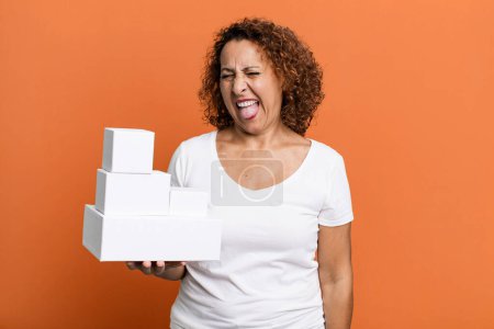 Photo for Pretty middle age woman with cheerful and rebellious attitude, joking and sticking tongue out. blank white boxes packaging - Royalty Free Image