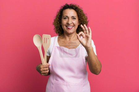 Foto de Pretty middle age woman feeling happy, showing approval with okay gesture. home wife chef concept - Imagen libre de derechos