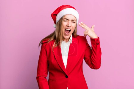 Foto de Pretty blonde woman looking unhappy and stressed, suicide gesture making gun sign. christmas and santa hat concept - Imagen libre de derechos