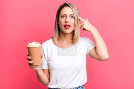 Photo for Pretty blonde woman feeling confused and puzzled, showing you are insane with a hot coffee - Royalty Free Image
