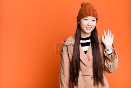 Foto de Pretty asian woman smiling happily, waving hand, welcoming and greeting you - Imagen libre de derechos