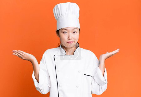 Téléchargez les photos : Pretty asian woman feeling puzzled and confused and doubting. restaurant chef concept - en image libre de droit