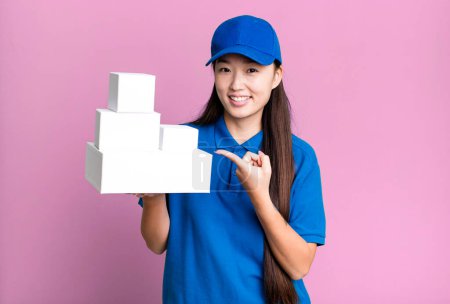 Foto de Pretty asian woman smiling cheerfully, feeling happy and pointing to the side. delivery packages concept - Imagen libre de derechos
