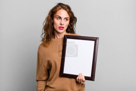 Foto de Mujer bonita hispana sintiéndose triste, molesta o enojada y mirando hacia un lado con un marco vacío - Imagen libre de derechos