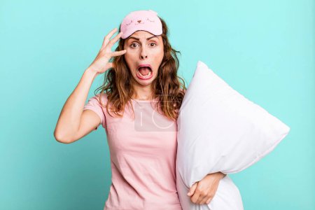 Photo for Hispanic pretty woman screaming with hands up in the air wearing pajamas and a pillow - Royalty Free Image