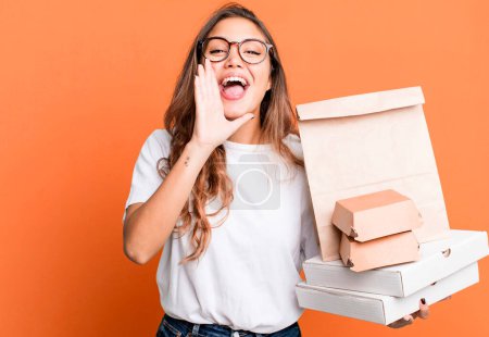 Photo for Hispanic pretty woman feeling happy,giving a big shout out with hands next to mouth. with fast food packages - Royalty Free Image