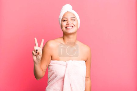 Téléchargez les photos : Hispanic pretty woman smiling and looking friendly, showing number two wearing bathrobe. beauty concept - en image libre de droit
