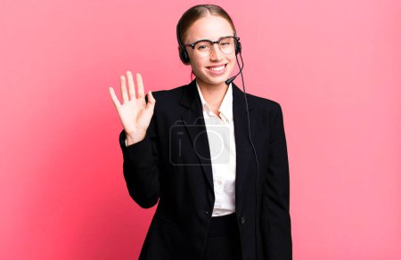 Téléchargez les photos : Jolie femme caucasienne souriant joyeusement, main agitant, vous accueillant et vous saluant. concept de télémarketing - en image libre de droit