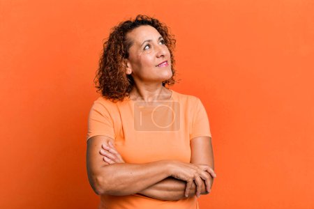 Foto de Mujer hispana de mediana edad sintiéndose feliz, orgullosa y esperanzada, preguntándose o pensando, mirando hacia arriba para copiar espacio con los brazos cruzados - Imagen libre de derechos