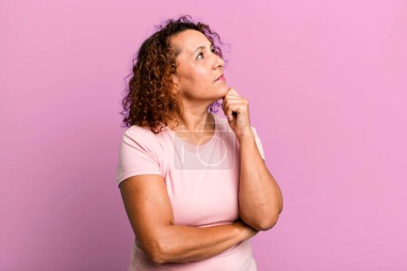 Téléchargez les photos : Femme hispanique d'âge moyen se sentant réfléchie, se demandant ou imaginant des idées, rêvant et regardant vers le haut pour copier l'espace - en image libre de droit