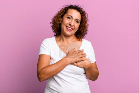 Photo for Middle age hispanic woman feeling romantic, happy and in love, smiling cheerfully and holding hands close to heart - Royalty Free Image