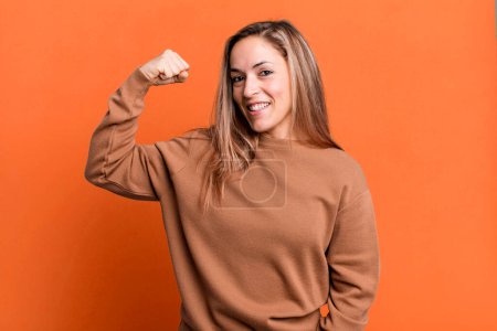 Photo for Blonde adult woman feeling happy, satisfied and powerful, flexing fit and muscular biceps, looking strong after the gym - Royalty Free Image