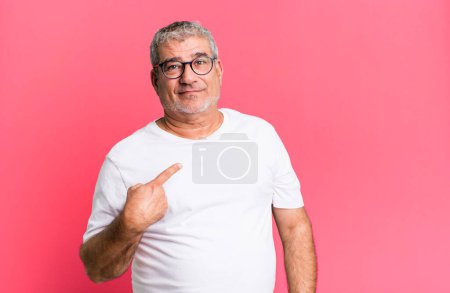 middle age senior man looking proud, confident and happy, smiling and pointing to self or making number one sign