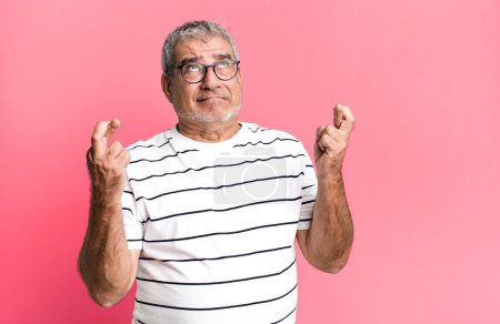 Téléchargez les photos : Homme âgé d'âge moyen croisant les doigts anxieusement et espérant bonne chance avec un regard inquiet - en image libre de droit