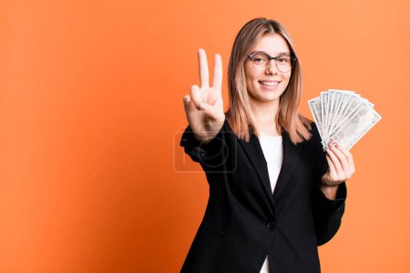 Foto de Joven bonita mujer sonriendo y buscando amigable, mostrando el número dos. concepto de negocio y dinero - Imagen libre de derechos
