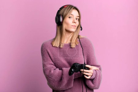 Foto de Young pretty woman shrugging, feeling confused and uncertain. gamer with headset and controller - Imagen libre de derechos