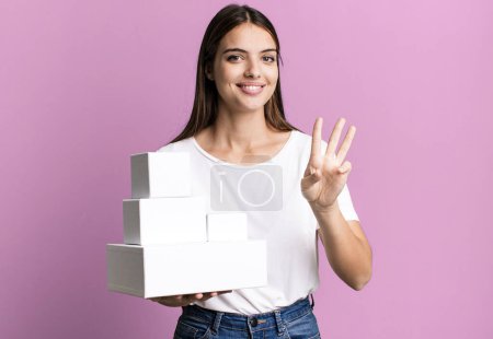 Téléchargez les photos : Jeune jolie femme souriante et sympathique, montrant le numéro trois. boîtes blanches vierges - en image libre de droit