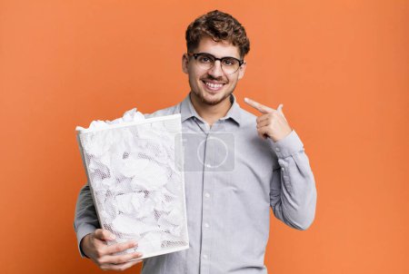 Foto de Young adult caucasian man smiling confidently pointing to own broad smile with a paper balls trash concept - Imagen libre de derechos