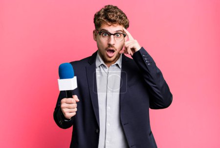 Photo for Young adult caucasian man looking surprised, realizing a new thought, idea or concept. journalist or presenter with a microphone - Royalty Free Image