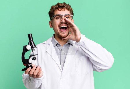 Foto de Young adult caucasian man feeling happy,giving a big shout out with hands next to mouth. scients laboratory student with a microscope concept - Imagen libre de derechos