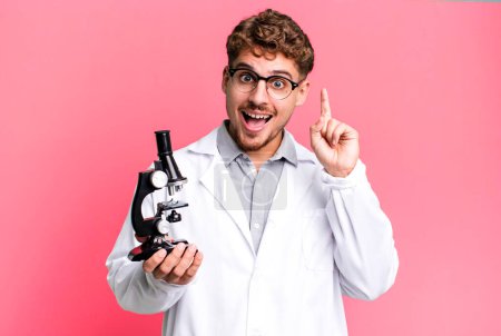 Téléchargez les photos : Young adult caucasian man feeling like a happy and excited genius after realizing an idea. scients laboratory student with a microscope concept - en image libre de droit