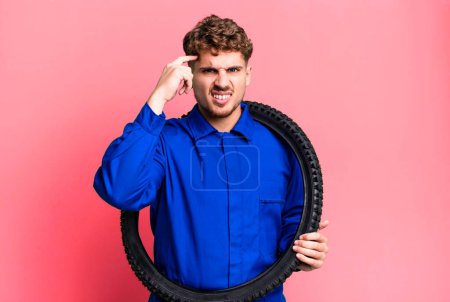 Foto de Young adult caucasian man feeling confused and puzzled, showing you are insane. bike repairman or mechanic concept - Imagen libre de derechos