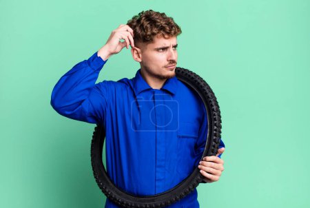 Photo for Young adult caucasian man smiling happily and daydreaming or doubting. bike repairman or mechanic concept - Royalty Free Image