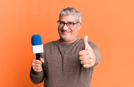 Photo for Middle age senior man feeling proud,smiling positively with thumbs up. journalist or tv presenter with a micro - Royalty Free Image